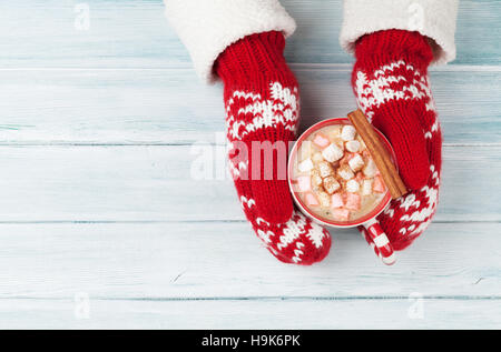 Female hands holding hot chocolate with marshmallow above wooden table. Top view with copy space Stock Photo