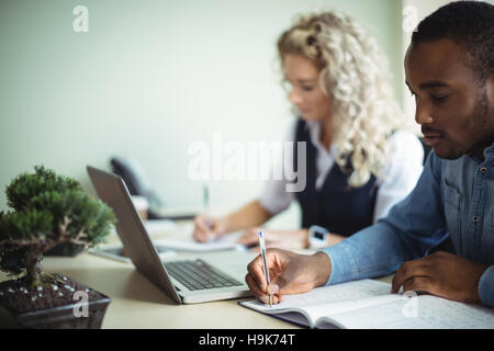 Business executive taking notes while using laptop Stock Photo