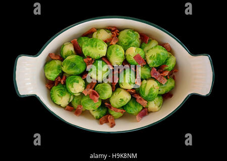 Fresh steamed brussels sprouts with crisp bacon bits in vintage serving dish isolated on black.  Shot in natural light from overhead perspective. Stock Photo