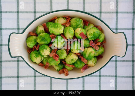 Fresh steamed brussels sprouts with crisp bacon bits in vintage serving dish on green and white fabric. Shot in natural light from overhead perspectiv Stock Photo