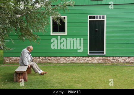 Lonely old man sits on a bench under a tree outside his home image in landscape format with copy space Stock Photo