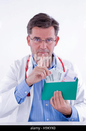 Doctor with money envelope pointing silencing finger to his mouth, symbolic of doctor's remuneration Stock Photo