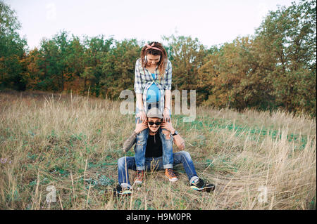 young guy in a cap solar oskah, with beard mustache, and tattooed, his pregnant girl in dreadlocks, outdoors the fall posing at the camera, Stock Photo