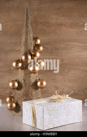 Decorative Christmas tree  made from straw  with golden balls and present box on wooden background. Stock Photo