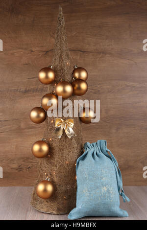 Decorative Christmas tree made from straw  with golden balls and blue jute gifts bag on wooden background Stock Photo