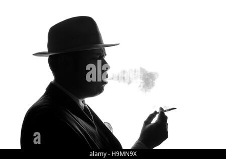 Silhouette of private detective lights cigarette. Agent looks like Al Capone stay side to camera. Police criminal scene in black and white. Gangster studio shot Stock Photo