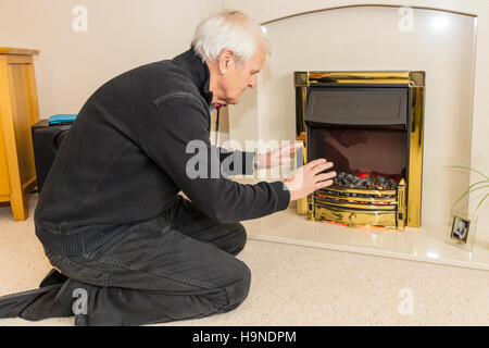 OAP trying to keep warm warming hands near fire keeping bills down cannot afford heating bill high gas energy bills UK England Stock Photo