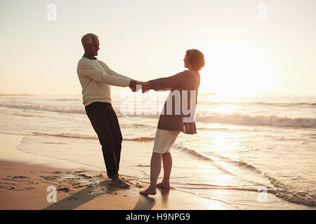 Loving senior couple holding hands and enjoying a romantic day at the sea shore. Senior man and woman couple holding hands at sunset on the beach. Stock Photo