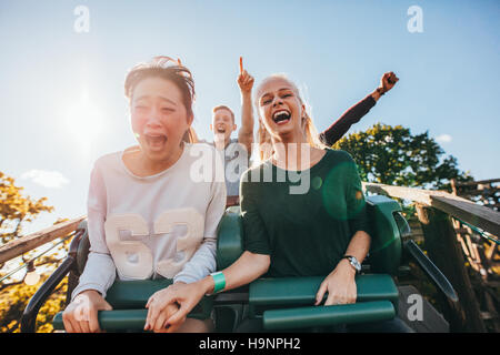 Enthusiastic young friends riding roller coaster ride at amusement park. Young people having fun at amusement park. Stock Photo