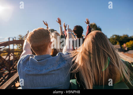 Rear view shot of young people on a thrilling roller coaster ride at amusement park. Group of friends having fun at fair and enjoying on a ride. Stock Photo