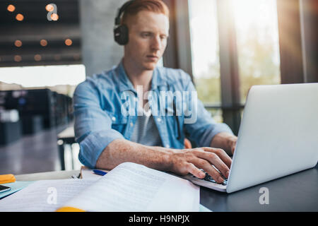 Male student in university library using laptop. Young man studying on school assignment. Stock Photo