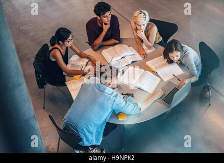 High angle shot of young men and women sitting at table with books using laptop. university students doing group study. Stock Photo