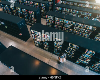 Top view of female student reading book while sitting at library bookshelf. university student studying in library. Stock Photo