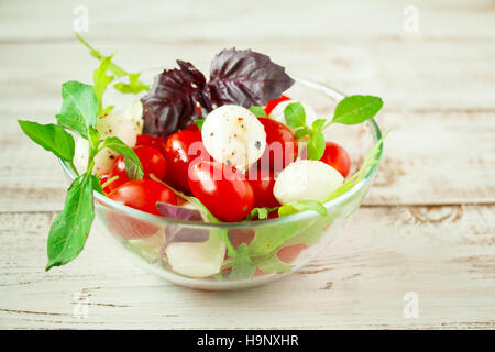 Tomatoes with mozzarella, arugula and basil on a white wooden background. Caprese salad. Stock Photo