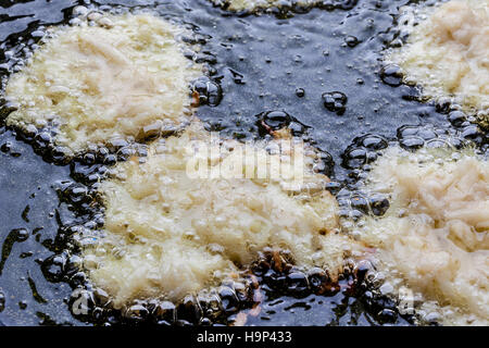 Frying latkes with raw side up in deep oil on pan from above closeup Stock Photo