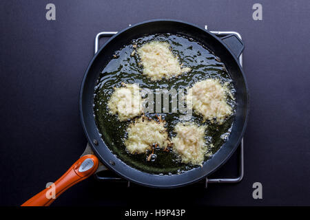 Frying latkes with raw side up in deep oil on pan on stove directly from above Stock Photo