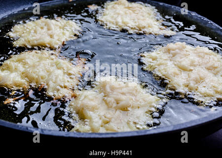 Frying latkes with raw side up in deep oil on pan from side closeup Stock Photo