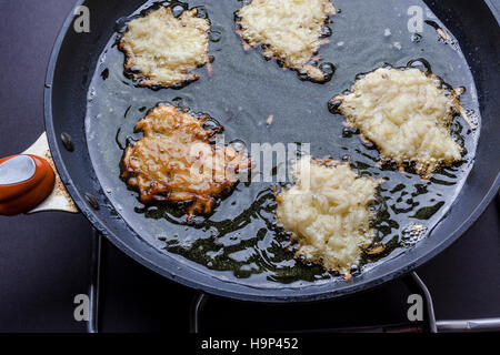 Frying latkes with raw side up and one turned in deep oil on pan on stove from above Stock Photo