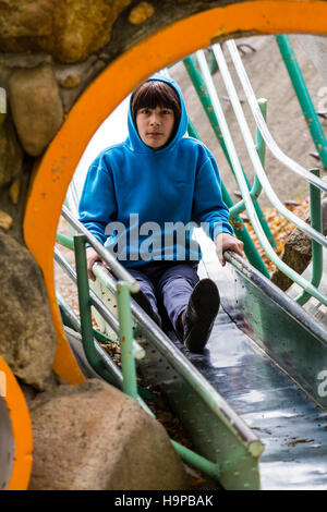 Japan, Akashi. Kazki, early teenage Caucasian boy, 13-14 years old, in blue hoodie sliding on slide in tunnel towards viewer. Eye-contact. Stock Photo