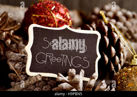 the text seasons greetings written in a black signboard and some pine cones and christmas balls Stock Photo