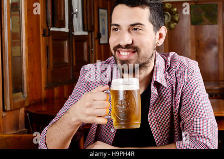 Portrait of young latin man drinking beer at a bar. Indoors. Stock Photo