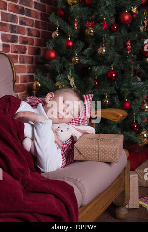 Boy sleeping under a blanket on the sofa near the Christmas tree with gifts Stock Photo