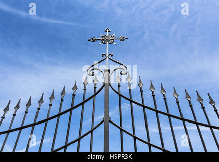 Wrought iron gate with cross against blue sky Stock Photo