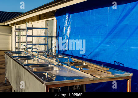 Old kitchen sink outside a public washroom that is being renovated. Blue tarp cover part of building. Stock Photo