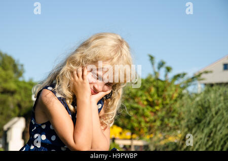 little blond girl in thinking posture holding her head with hands Stock Photo