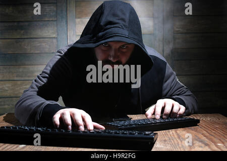 hacker in the black hood in a room with wooden walls Stock Photo
