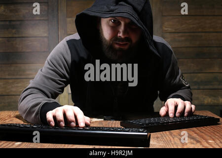 hacker in the black hood in a room with wooden walls Stock Photo