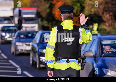 Belfast, Northern Ireland. 24 Nov 2016 - An armed PSNI officer waves on traffic during a vehicle checkpoint. Credit:  Stephen Barnes/Alamy Live News