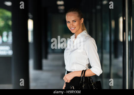 Young smiling businesswoman standing and holing handbag outdoors Stock Photo