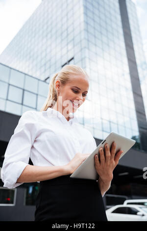 Young smiling business woman using tablet standing at the office building outdoors Stock Photo