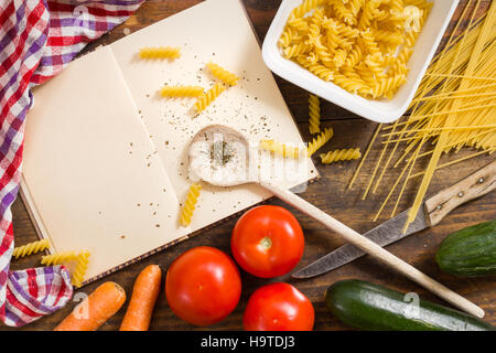 Opened cookbook with blank pages and noodles, cooking utensils, vegetable - top view still life with copy space on rustic wood Stock Photo