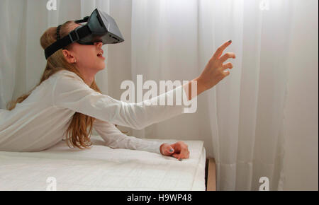 Girl in Virtual Reality headset looking up and trying to touch objects in virtual environment. Stock Photo