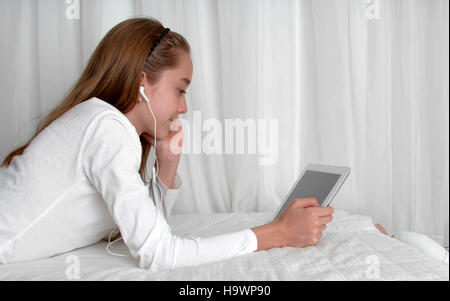 Teenager girl wearing earphone playing on tablet and listening music Stock Photo
