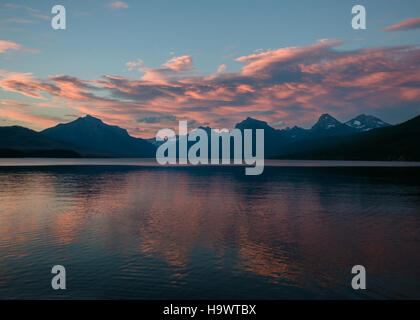 A fiery sunset over Glacier National Park paints the sky with vibrant colors, highlighting the park's rugged landscapes and natural beauty. This national park, known for its glaciers, peaks, and wildlife, offers visitors a stunning view of the changing sky and its surrounding natural environment, a testament to the park's ecological importance and scenic value. Stock Photo