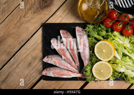 raw red mullet served on curly salad on slate plate on wooden table Stock Photo