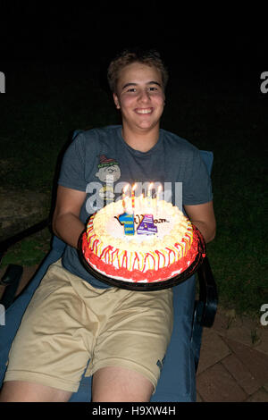 Teenage boy holds his year 14 happy birthday cake with burning candles. St Paul Minnesota MN USA Stock Photo