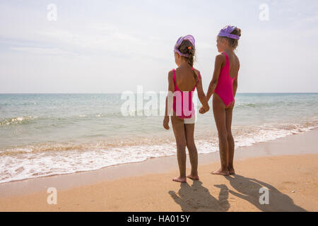 Two girls in bathing suits standing on the beach and look at the horizon