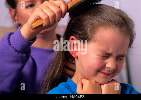Early morning before school mother combing daughters hair ( 6 years old) with girl in pain Marysville Washington State USA MR Stock Photo