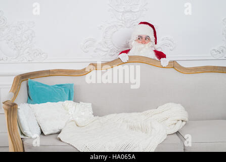 Santa Claus hiding behind a sofa over home interior Stock Photo