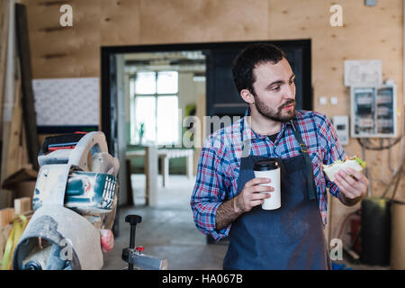 Cheerful carpentry worker having lunch eating sandwich in a workshop Stock Photo