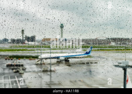 View from the lounge's glass windows covered by droplets in Haneda Airport of an airplane waiting under the rain Stock Photo