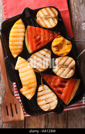 Delicious fruit apples, melon, pear, watermelon and peach on a grill pan close-up on the table. vertical view from above Stock Photo