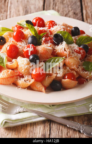 Conchiglie with tomatoes, olives and parmesan cheese on a plate close-up. vertical Stock Photo