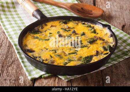 Hot scrambled eggs with spinach, cheddar cheese and mushrooms in a frying pan close-up on the table. horizontal Stock Photo