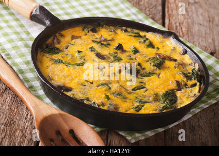 fritatta with spinach, cheddar cheese and mushrooms in a frying pan close-up on the table. Horizontal Stock Photo