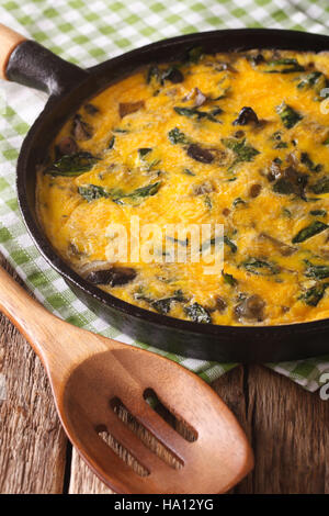 fritatta with spinach, cheddar cheese and mushrooms in a frying pan close-up on the table. Vertical Stock Photo